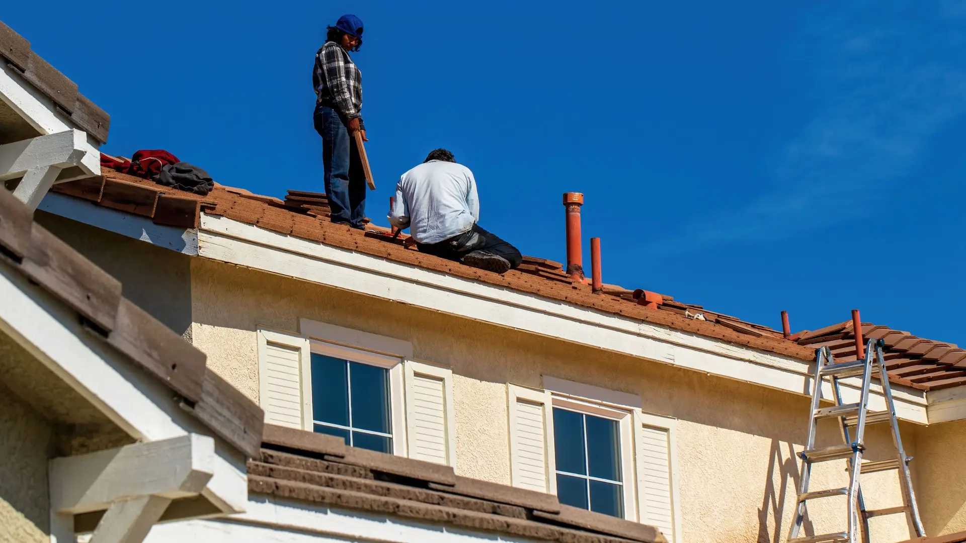 Roofers working on a tile roof of a stucco home in Southern California