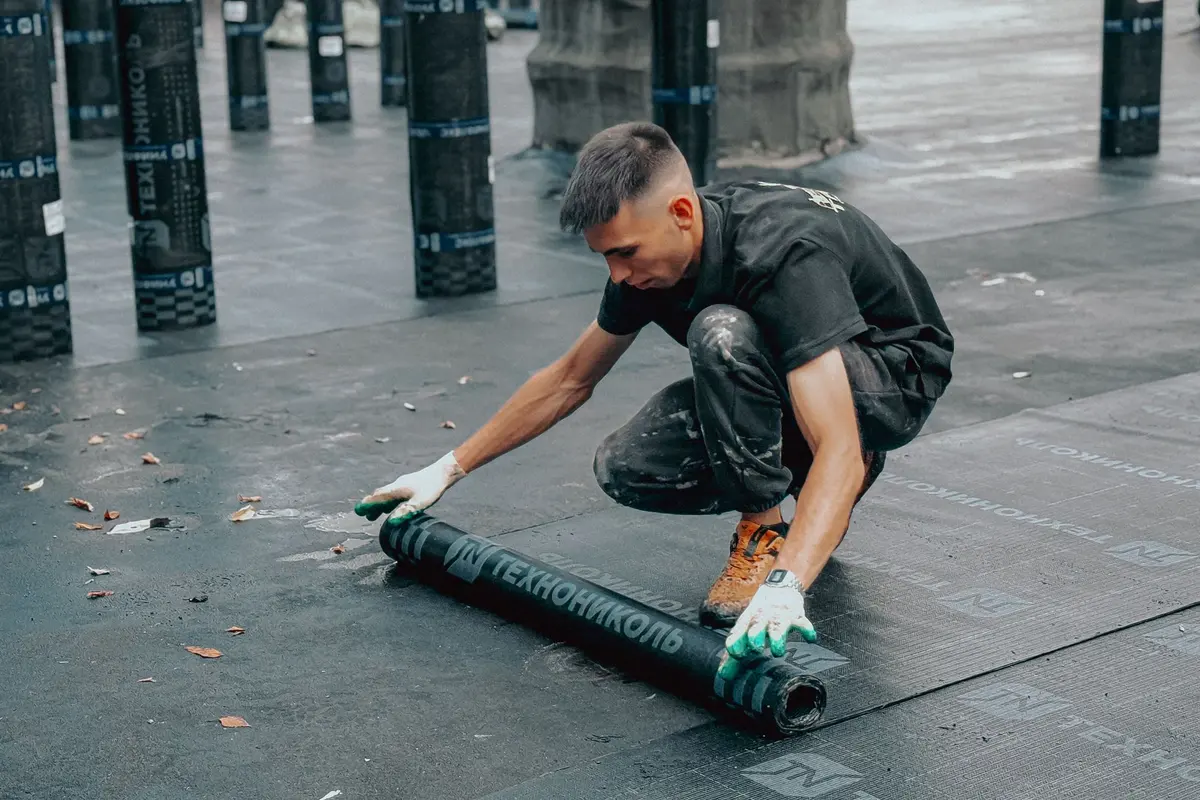 Roofer rolling out a modified bitumen membrane on a flat roof in Los Angeles, CA
